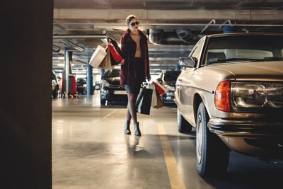 一名妇女提着购物纸袋朝停车场内的米色汽车走去
